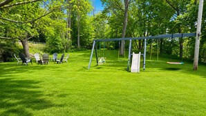 A grassy outdoor area with a swing set, chairs, and a slide.