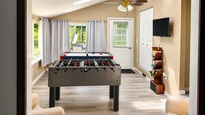 A room with a foosball table, a ceiling fan, a television, and a bookshelf.