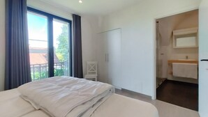 A hotel room with a bed, a small white chair, a wardrobe, a bathroom with a mirror and towel, and a view of the outside. - Stunning home in Oostduinkerke with WiFi (Oostduinkerke)