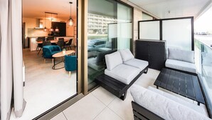 Ein stilvoller Wohnbereich mit einer Couch, einem Esstisch und Stühlen, ein Balkon mit Blick auf die Stadt und eine Küche im Hintergrund.