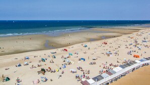 Ein Strand mit vielen Liegen und Sonnenschirmen, ein klarer Himmel und das Meer im Hintergrund.