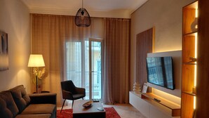 Ein modernes Wohnzimmer mit Sofa, Sessel, Fernseher und einem roten Teppich.
