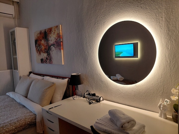 Ein modernes Hotelzimmer mit einem Bett, einem Schreibtisch mit Lampe, einem Fernseher und einem Wandbild.