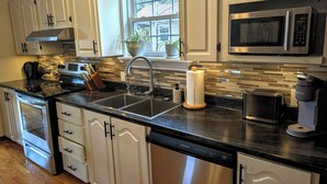A modern kitchen with white cabinets, a stainless steel range, a double sink, and a window with a view of the outside. - Cozy cottage located just over an hour to St. John's, NL! Pets welcome! (Placentia)