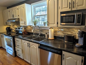 Una cocina moderna con gabinetes blancos, una estufa de acero inoxidable, un lavamanos doble y una ventana con vistas al exterior.