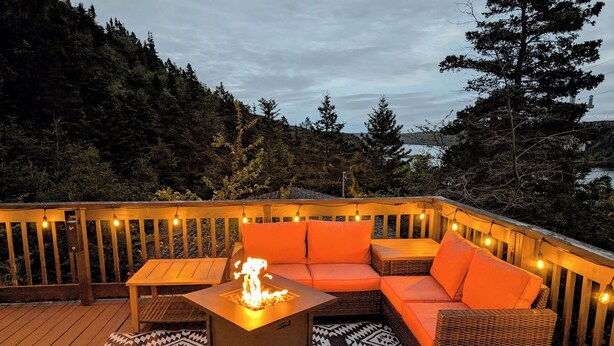 A deck with a fire pit, orange seating, and string lights. - Cozy cottage located just over an hour to St. John's, NL! Pets welcome! (Placentia)