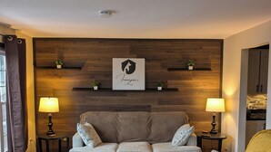 A modern living room with a sofa, two side tables with lamps, a coffee table, and a wooden accent wall. - Cozy cottage located just over an hour to St. John's, NL! Pets welcome! (Placentia)