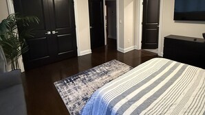 Un dormitorio con cama, televisor, planta y dos puertas.