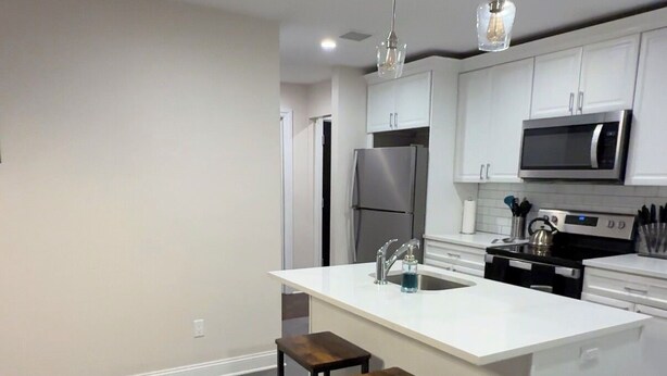 Una cocina moderna con una isla central, taburetes de bar, microondas y un refrigerador de acero inoxidable.