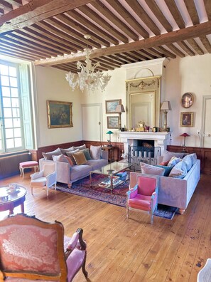 Une pièce avec des poutres en bois, un lustre, une cheminée et divers meubles, notamment des canapés et des fauteuils.