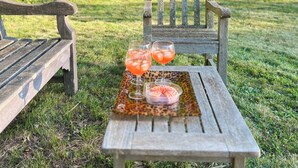 A wooden bench and table with two glasses of a red beverage and a small container of food in a natural outdoor setting. - Charming 17th-Century French Manor (Le Breuil-en-Bessin)