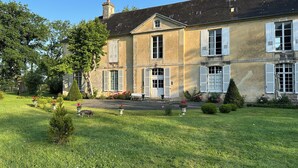 A large, two-story building with a symmetrical facade, multiple windows with shutters, and a well-maintained lawn with small trees and flower beds. - Charming 17th-Century French Manor (Le Breuil-en-Bessin)
