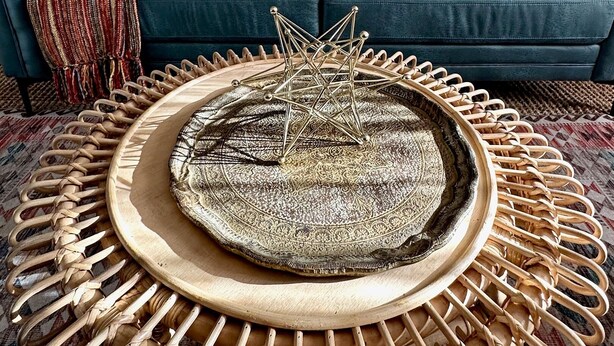 Un salon avec une table basse ronde en fibres tressées, un canapé bleu foncé agrémenté de coussins à motifs et deux œuvres d’art murales.