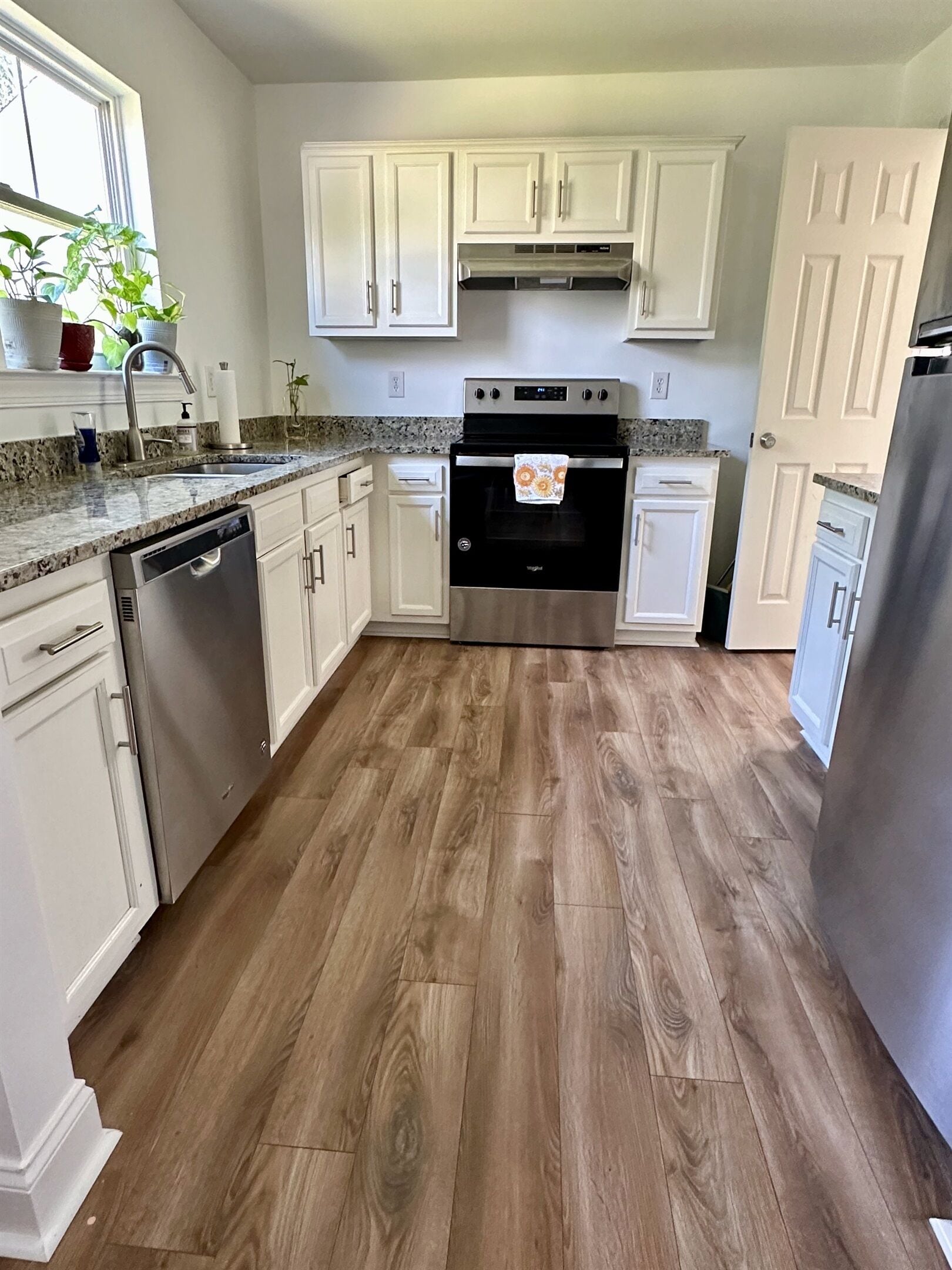 A kitchen with white cabinets, a stainless steel dishwasher, a black oven, and a granite countertop.