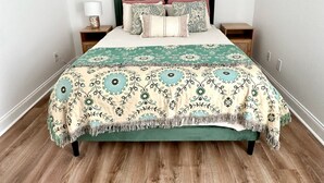 Un lit bien fait, recouvert d’une couvre-lit à motifs, deux tables de chevet avec des lampes et un plancher en bois.