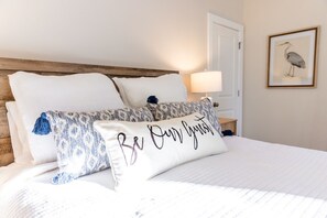 A bed with white bedding and decorative pillows, a wooden headboard, a bedside table with a lamp, and a framed picture on the wall. - The Alley Hideaway- Walk to shops and restaurants (Wilmington)