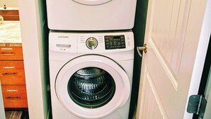 Una lavadora y secadora apiladas en un cuarto de lavado con piso de madera y una puerta blanca.