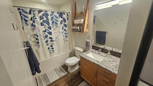 Un baño con cortina de ducha, inodoro, lavabo y armarios de madera.