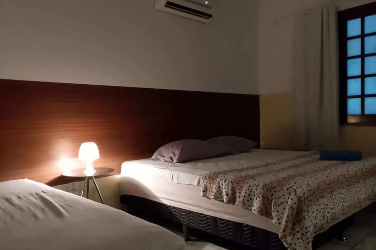 A hotel room with a bed, bedside table, lamp, and a window.