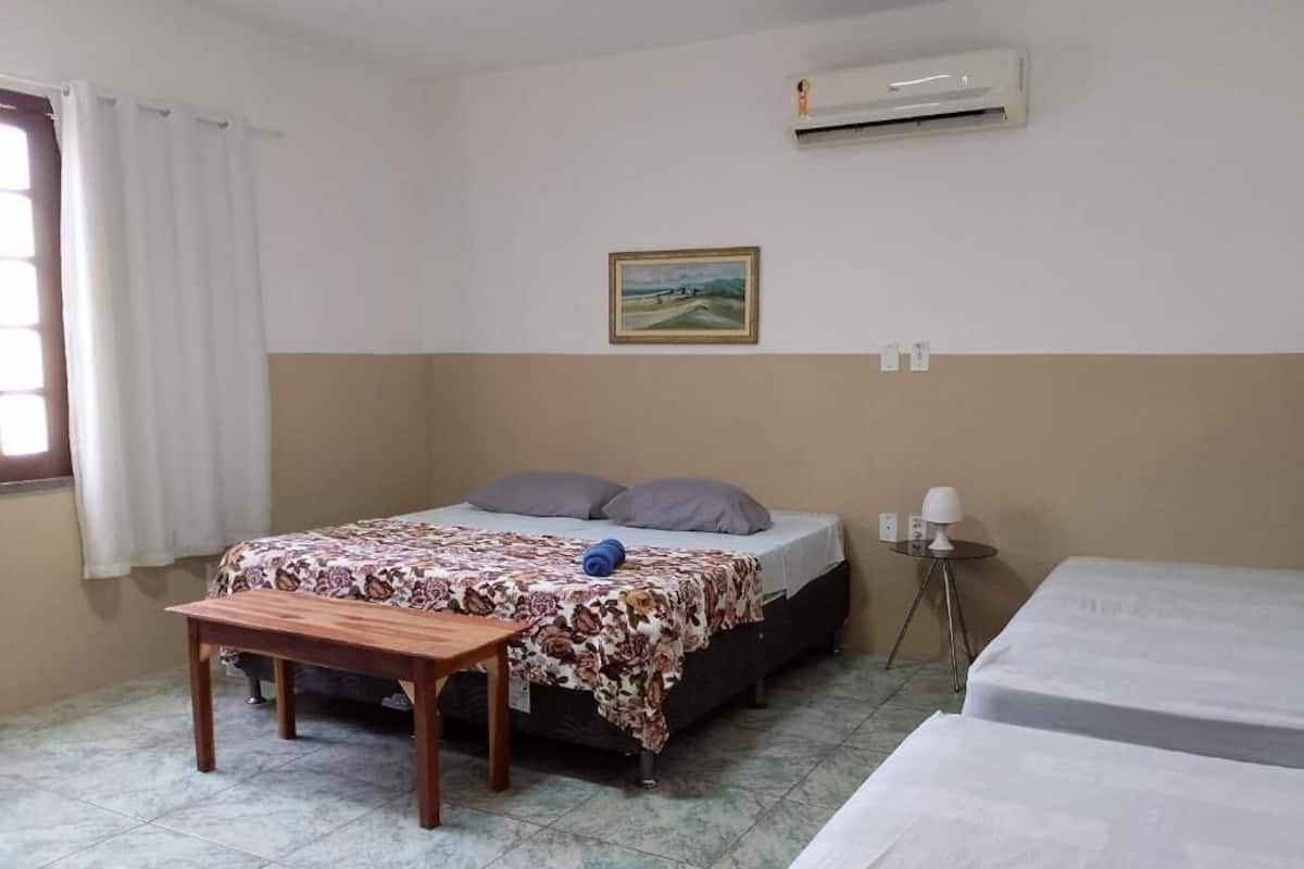 A room with a bed, a small table, a bedside lamp, and an air conditioning unit.
