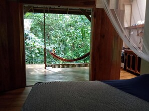 A room with a bed, a hammock, and a view of lush greenery outside. - Jungle Paunch Cabins (Bocas del Toro)