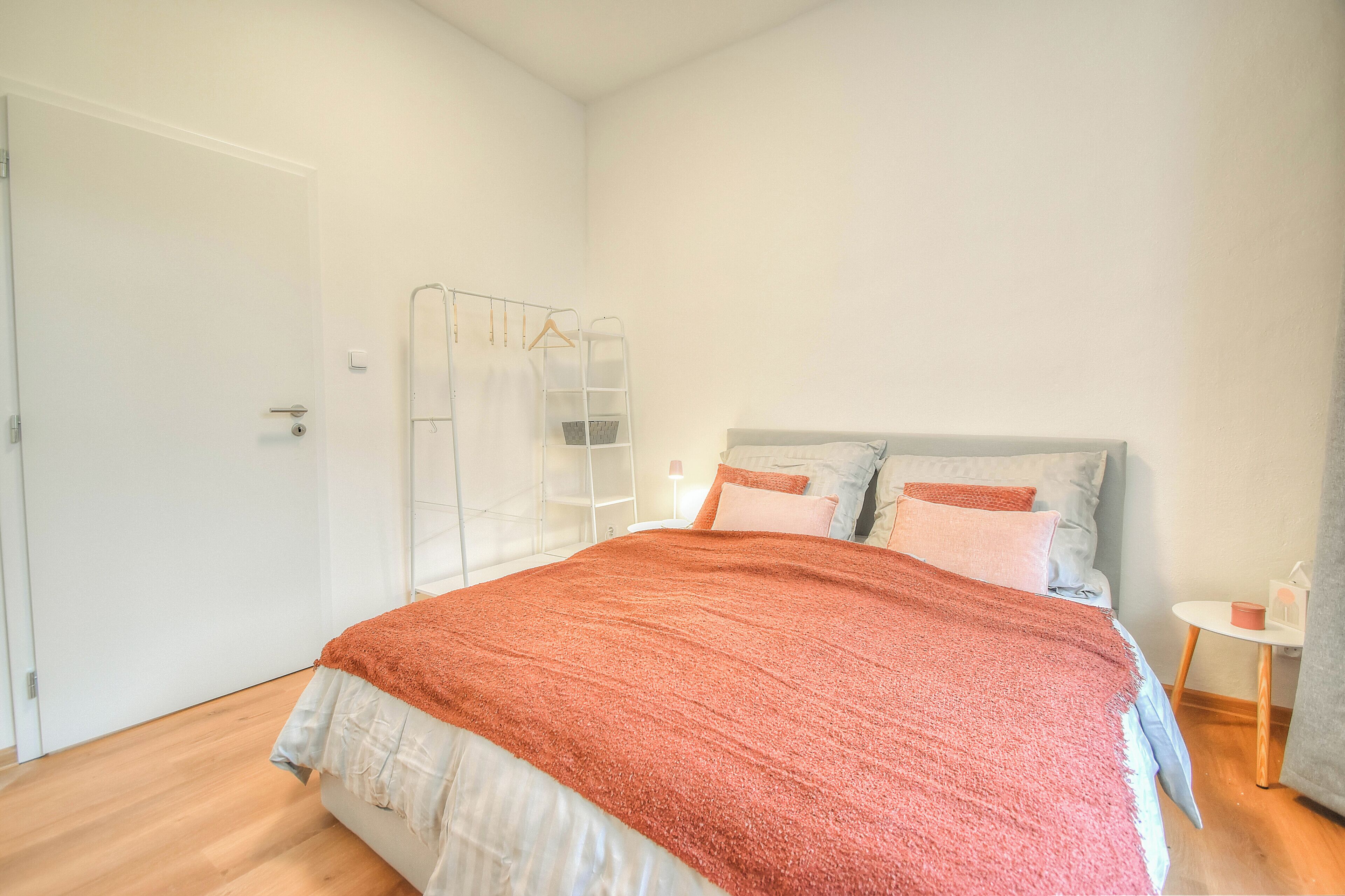 A bedroom with a bed, a wardrobe, a bedside table, and a lamp.