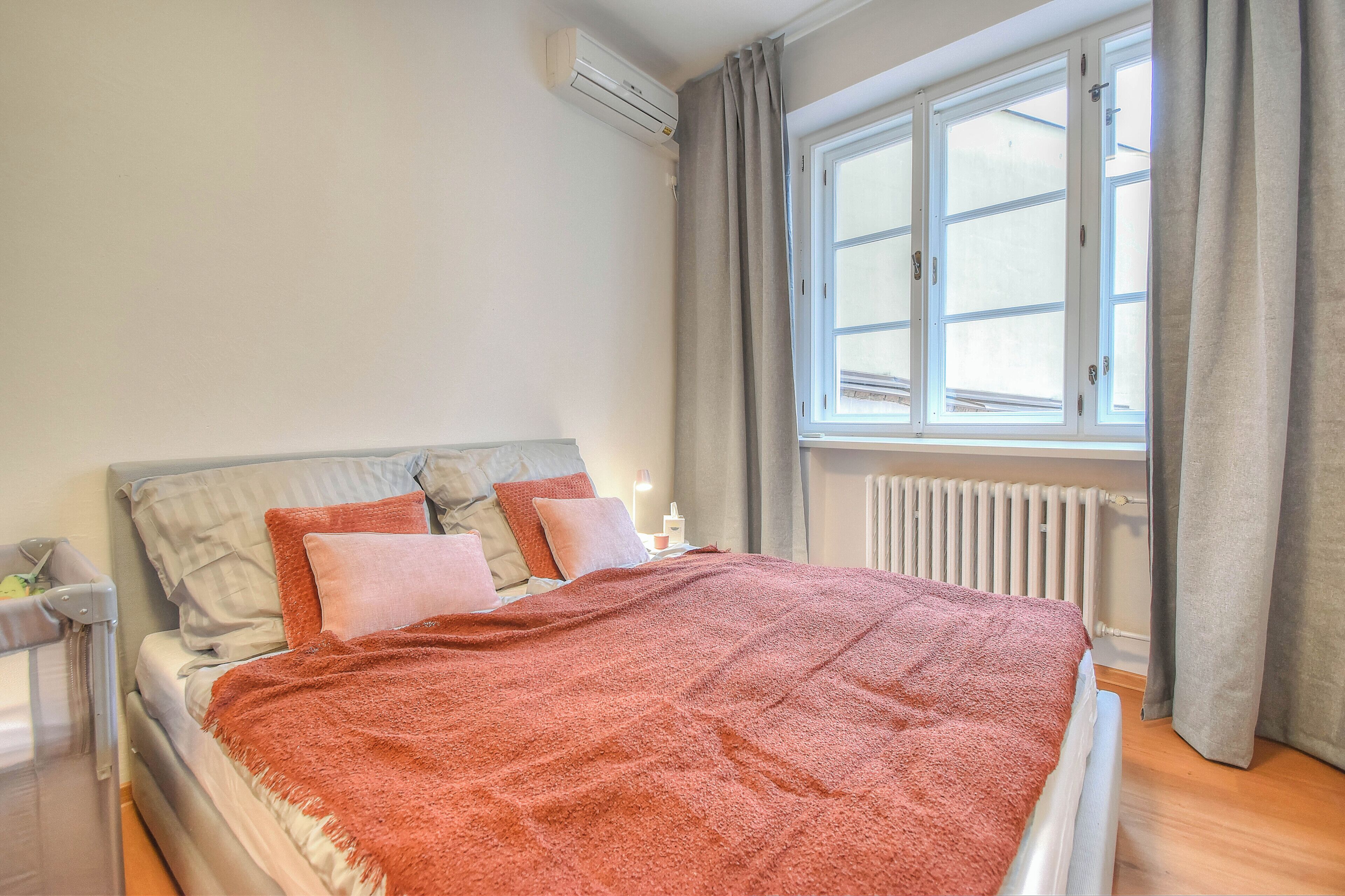 Un dormitorio con cama, ventana, radiador y equipo de aire acondicionado.