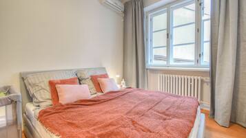 Un dormitorio con cama, ventana, radiador y equipo de aire acondicionado.