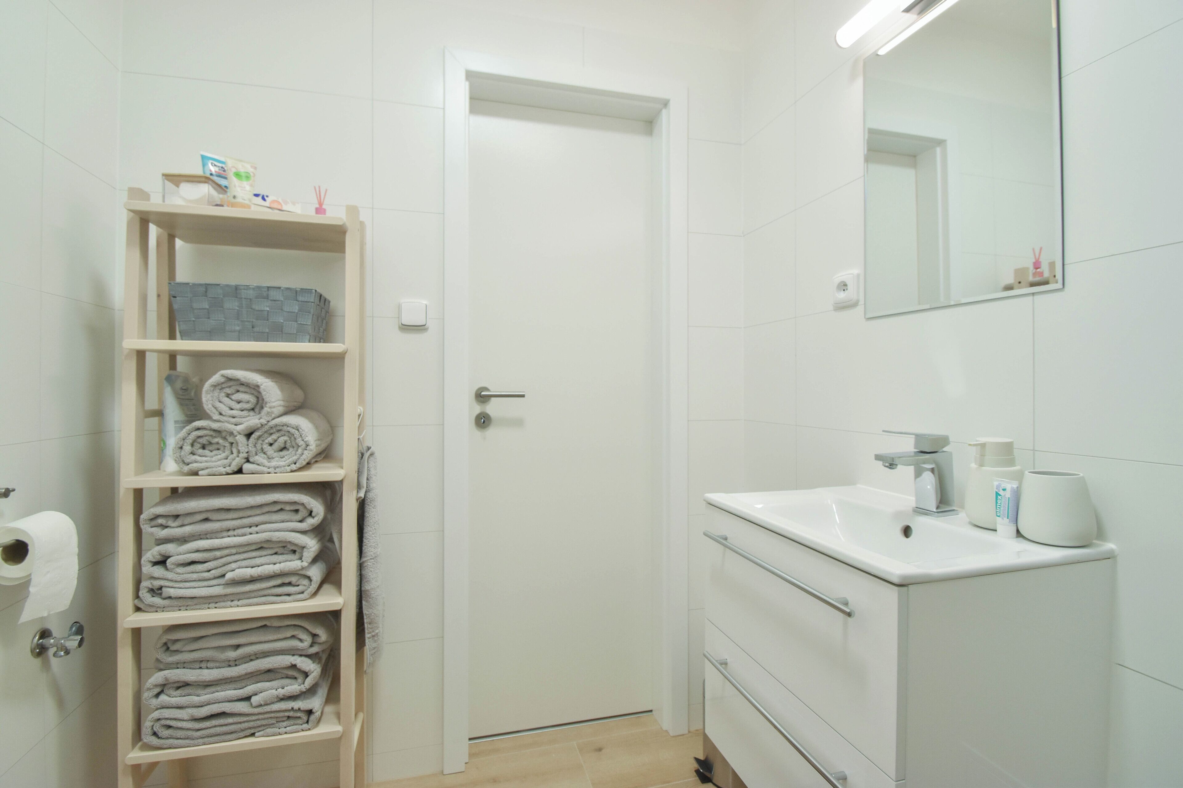 A bathroom with a white sink, mirror, and shelves with towels.