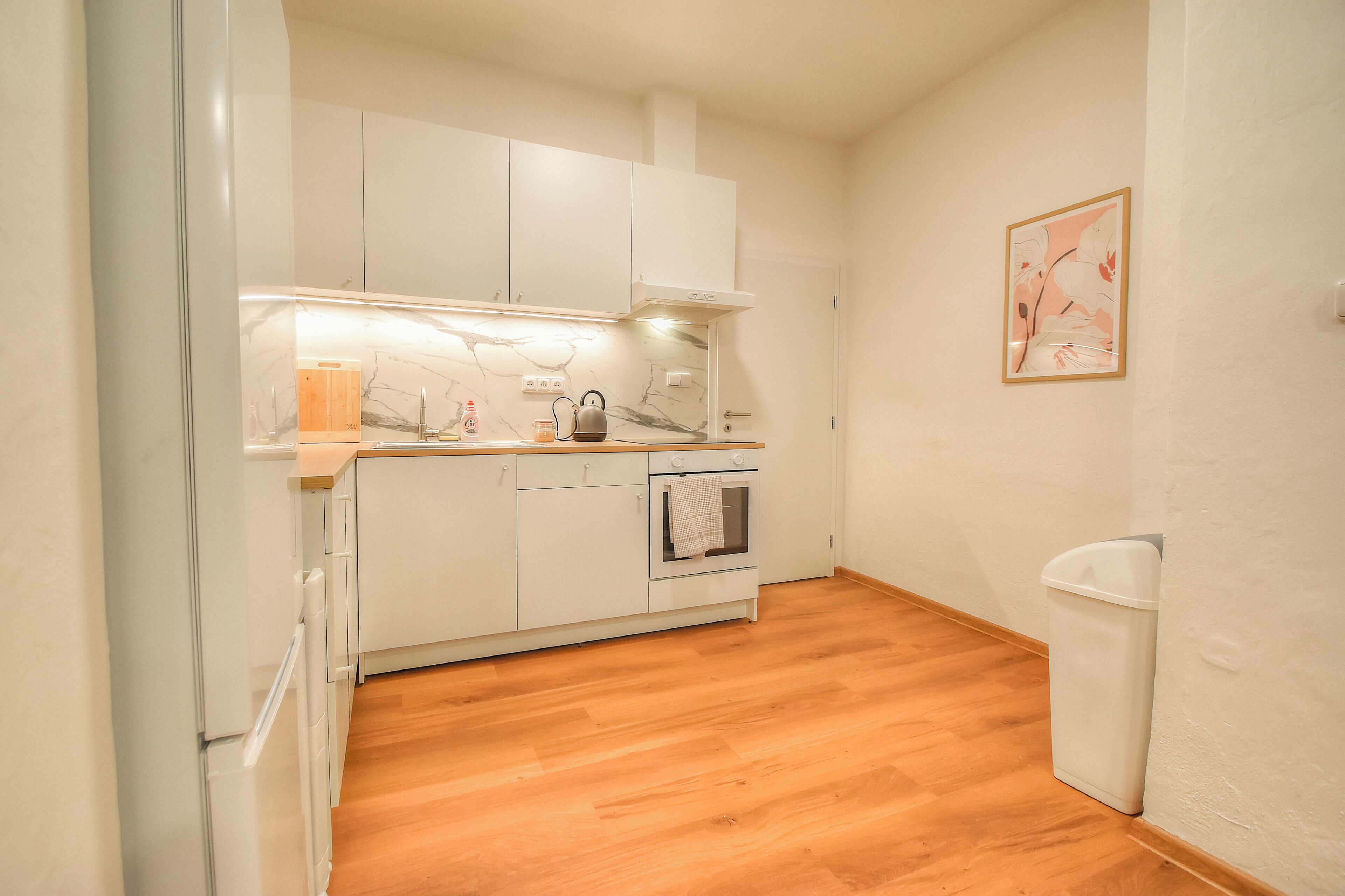 A compact kitchen with white cabinets, a wooden countertop, a built-in oven, and a trash bin.
