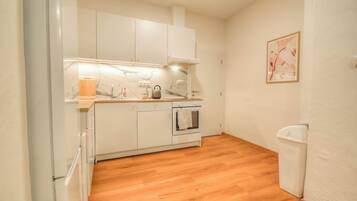 A compact kitchen with white cabinets, a wooden countertop, a built-in oven, and a trash bin.