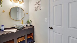 A bathroom with a round mirror, a sink with a decorative bowl, a towel, a wall-mounted light fixture, a door, and a decorative wall piece. - Escape to Nature! Cozy Blue Ridge Mtn Retreat (Epworth)