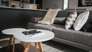 A modern living room with a grey sofa, two white round tables, and a kitchen in the background.