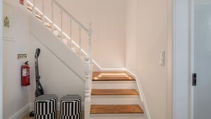 Una escalera con barandas blancas y escalones de madera, un extintor y dos otomanos a rayas.