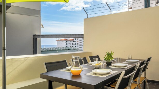 Un comedor con una mesa dispuesta para cuatro personas, una jarra de jugo de naranja y una planta en maceta.