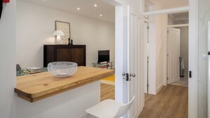 Una cocina moderna con encimera de madera, sillas blancas, una cesta y un televisor.