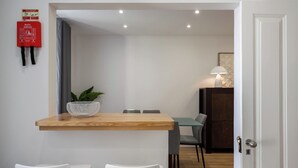 Un comedor con una mesa de madera, dos sillas blancas, una planta y un extintor en la pared.