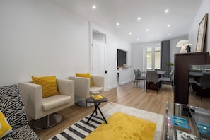 A modern living room with a sofa, armchair, and a small table with books. There is a dining area with chairs and a table in the background. - Rua do Pina 5 – Cozy 3-Bedroom Home in Funchal (Funchal)