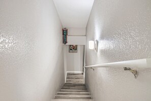 Un couloir étroit avec un escalier en bois menant à une pièce. Une enseigne au néon indique « ARGADE », et une affiche fait la publicité d’une « SALLE DE JEUX ».