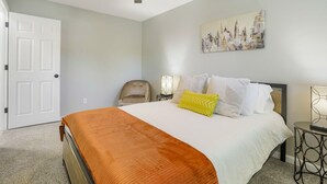 Un dormitorio con cama, una silla, un cuadro y un ventilador de techo.