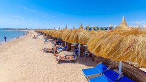A beach with rows of thatched umbrellas and lounge chairs, a sandy shore, and a clear blue sky. - Titanic Royal Palace (Hurghada)