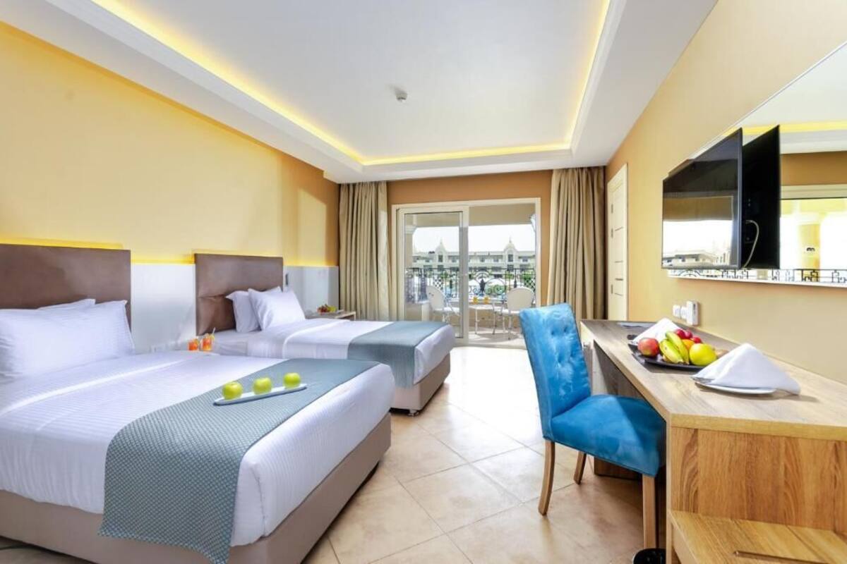 A hotel room with two beds, a desk, a chair, a TV, and a balcony with a view.