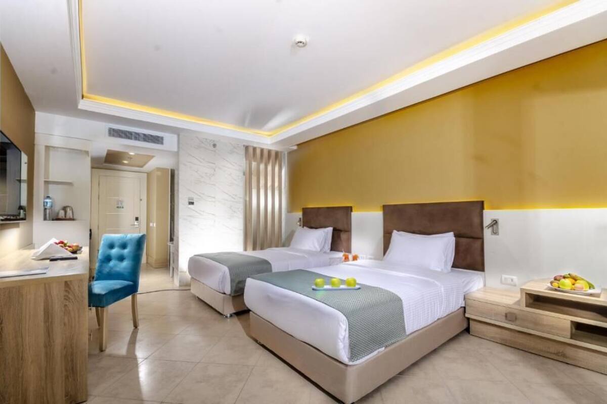 A hotel room with two beds, a desk, a chair, and a TV.