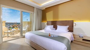 A hotel room with a large bed, a balcony with chairs, and a view of the city. - Titanic Royal Palace (Hurghada)