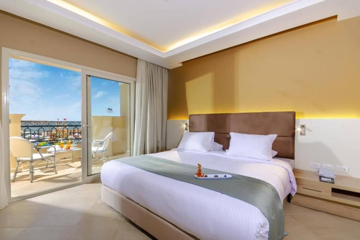 A hotel room with a large bed, a balcony with chairs, and a view of the city.