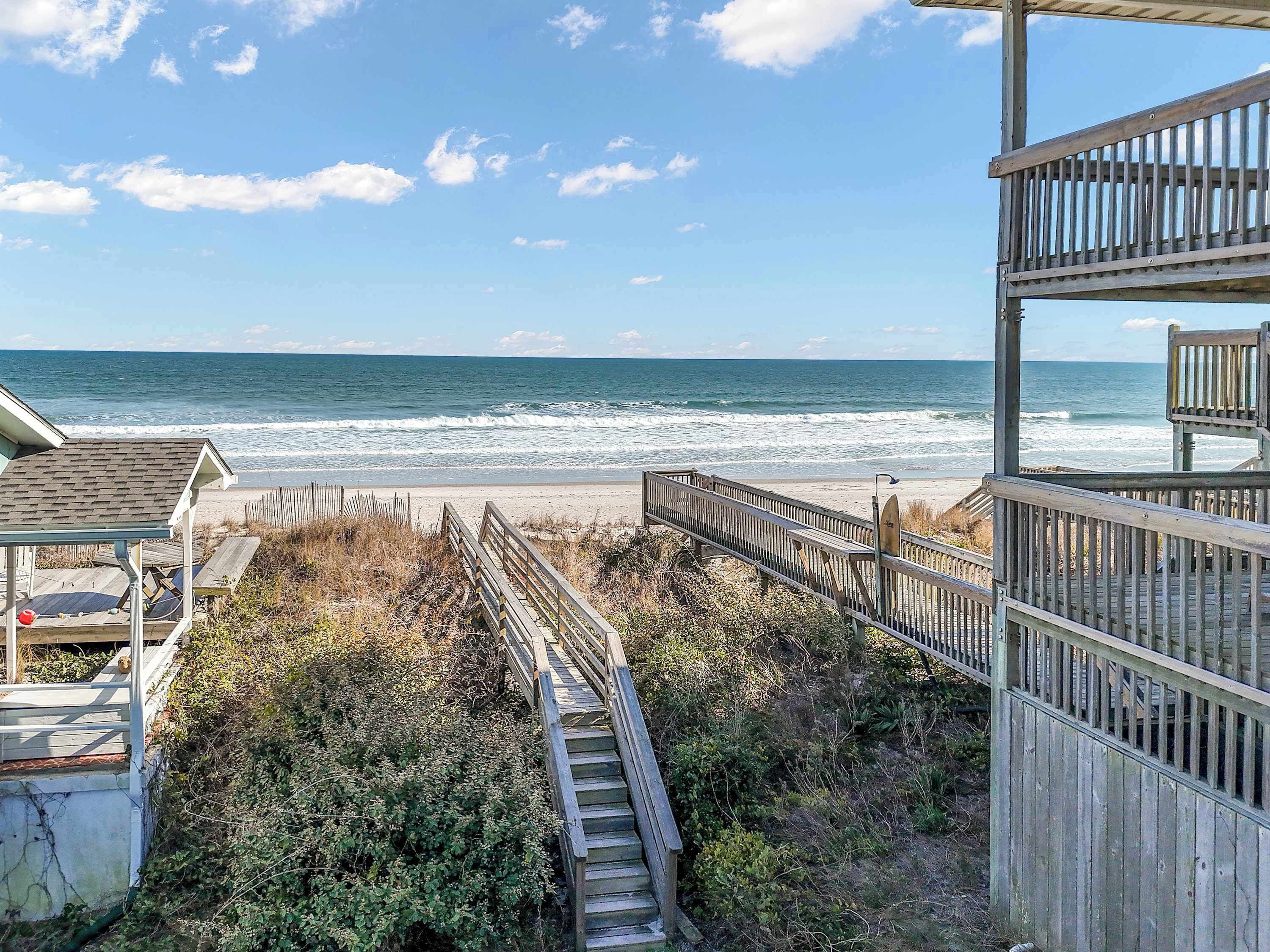 A wooden boardwalk leading to a beach with a view of the ocean.