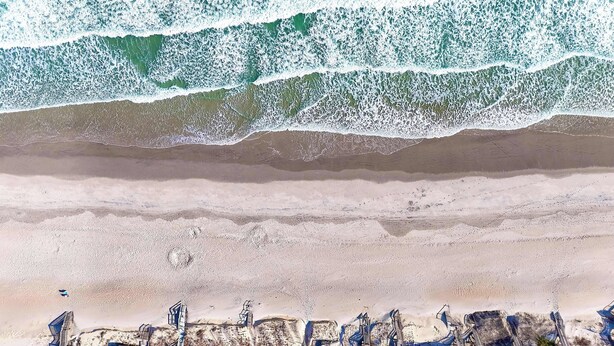 An aerial view of a coastal hotel with multiple buildings, a sandy beach, and waves crashing onto the shore. - Pirates & Paradise: Private Pool, Home Theatre, and Pet Friendly (Surf City)
