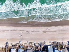 Vista aérea de un hotel costero con varias construcciones, una playa arenosa y olas rompiendo en la orilla.