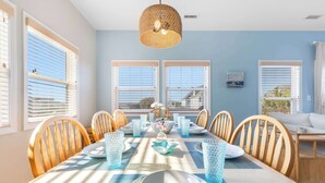 A dining area with a table set for six, wooden chairs, a woven pendant light, and large windows with blinds. - Pirates & Paradise: Private Pool, Home Theatre, and Pet Friendly (Surf City)
