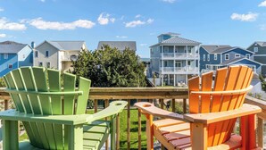 A deck with colorful Adirondack chairs, a wooden railing, and a view of houses in the background. - Pirates & Paradise: Private Pool, Home Theatre, and Pet Friendly (Surf City)